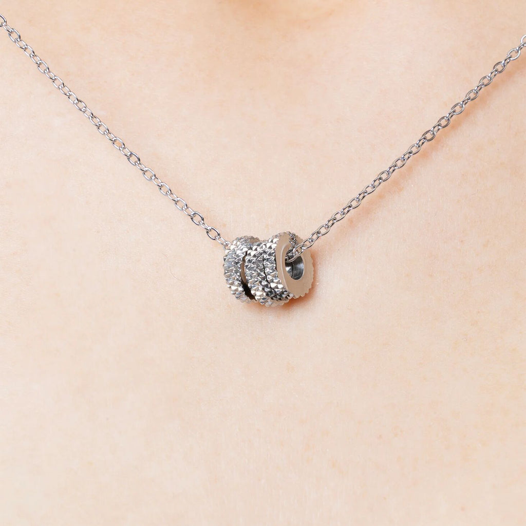 Silver necklace with textured spacer beads on a beige background