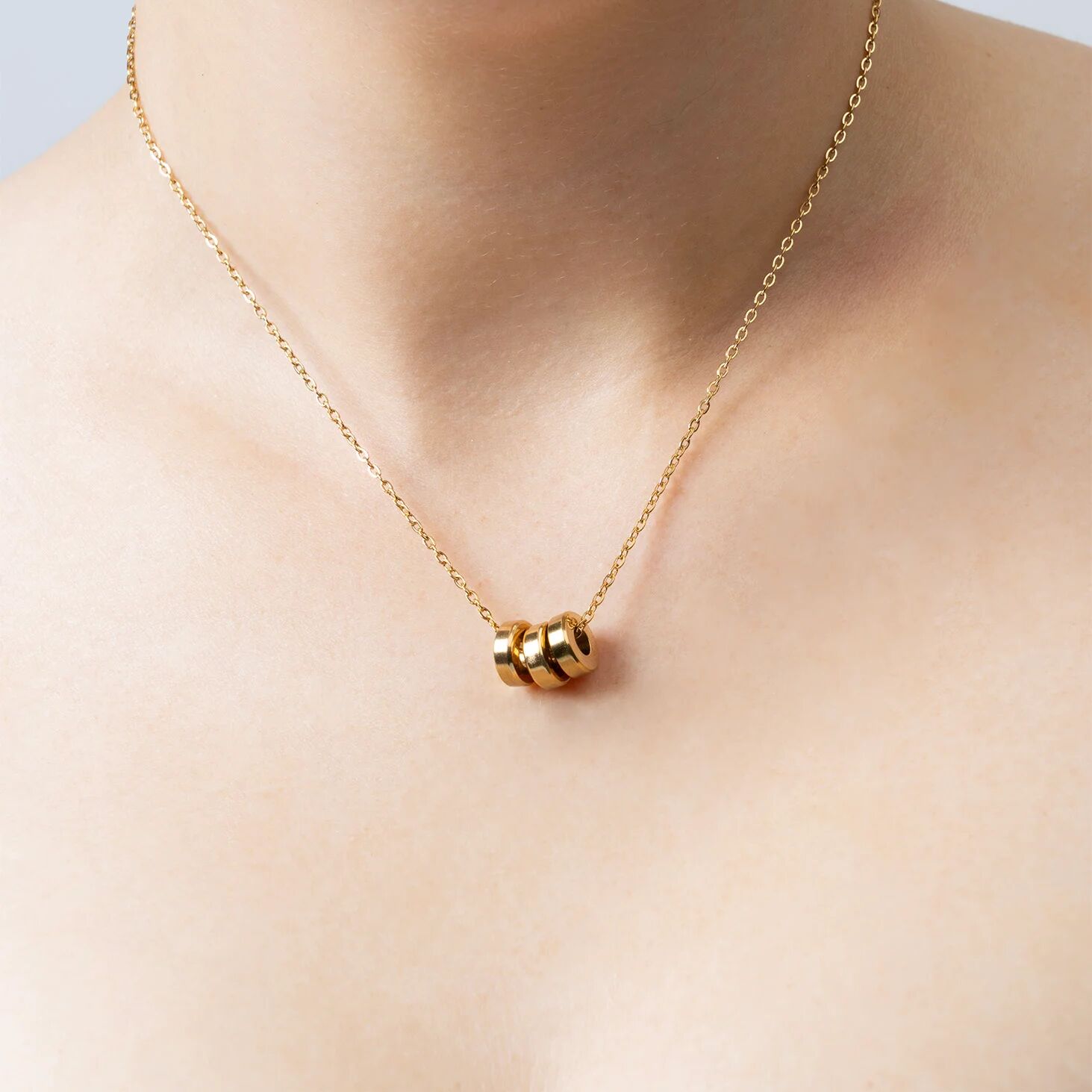 Gold necklace with spacer bead on a person's neck against a neutral background
