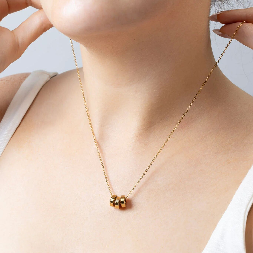 Gold necklace with a spacer bead on a person wearing a white top against a light background