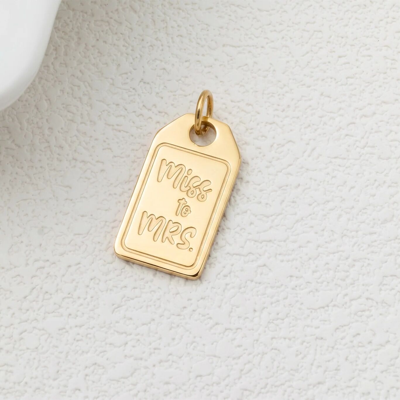 Gold pendant with 'Miss to Mrs.' engraving on a light gray textured background