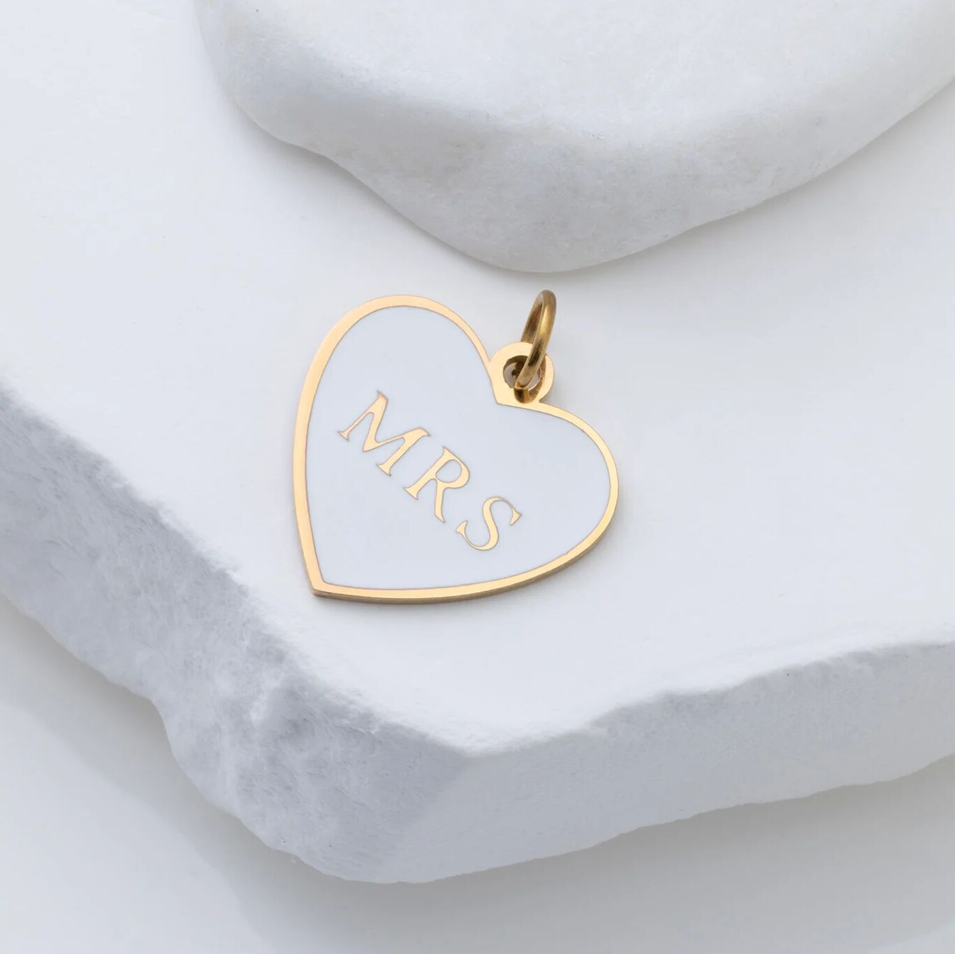 Heart-shaped gold pendant with 'MRS.' engraving on a white marble surface