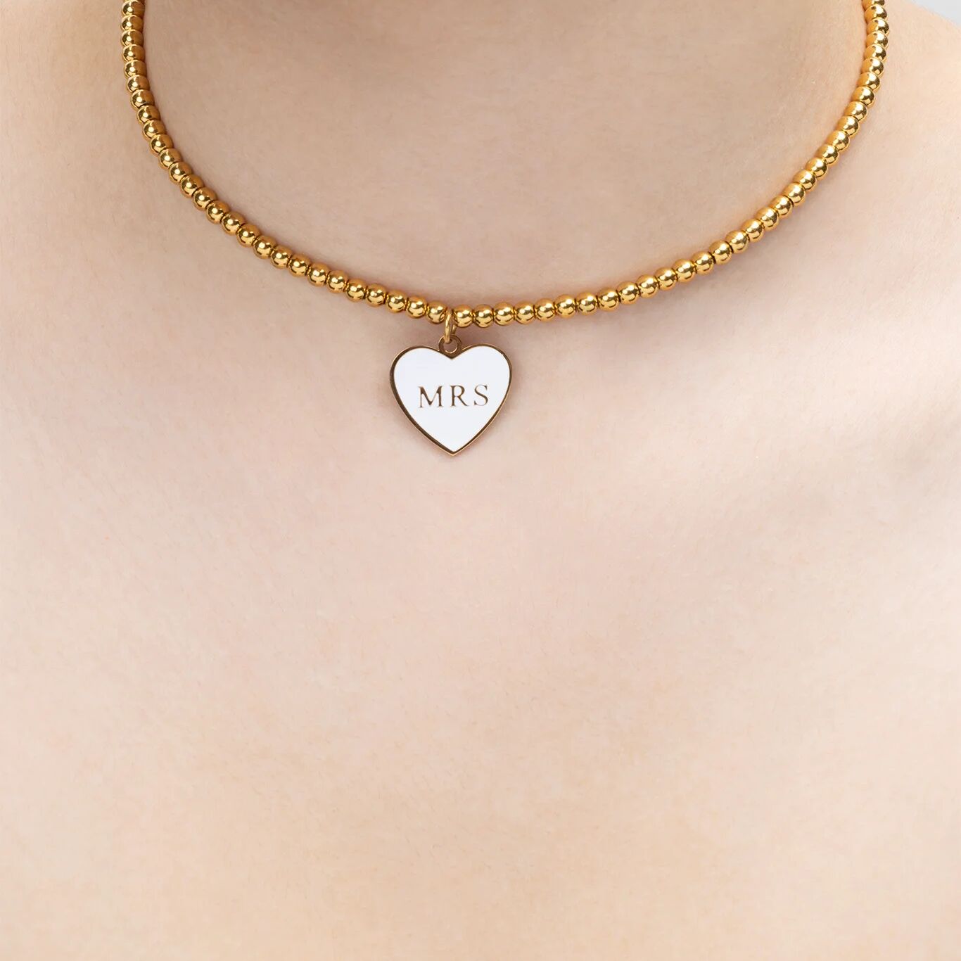 Gold necklace with a heart-shaped 'MRS' pendant on a plain background