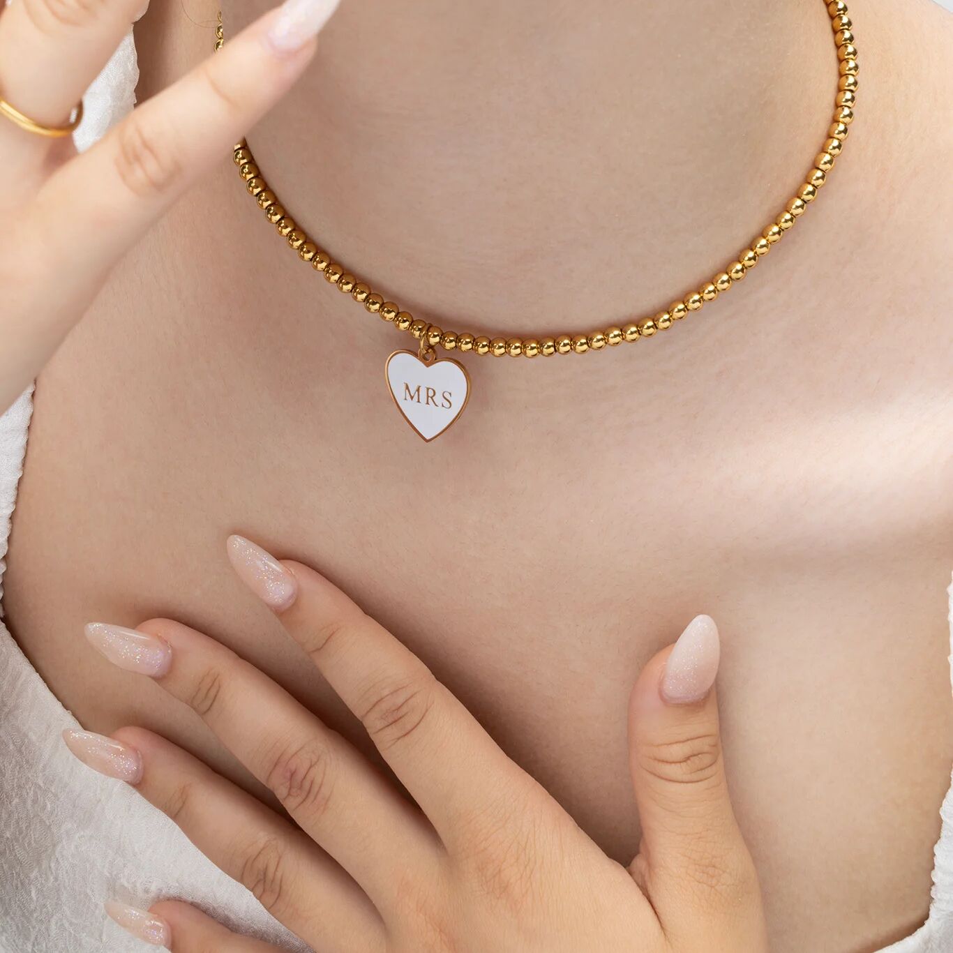 Gold necklace with a heart-shaped 'MRS' pendant on a person's chest.