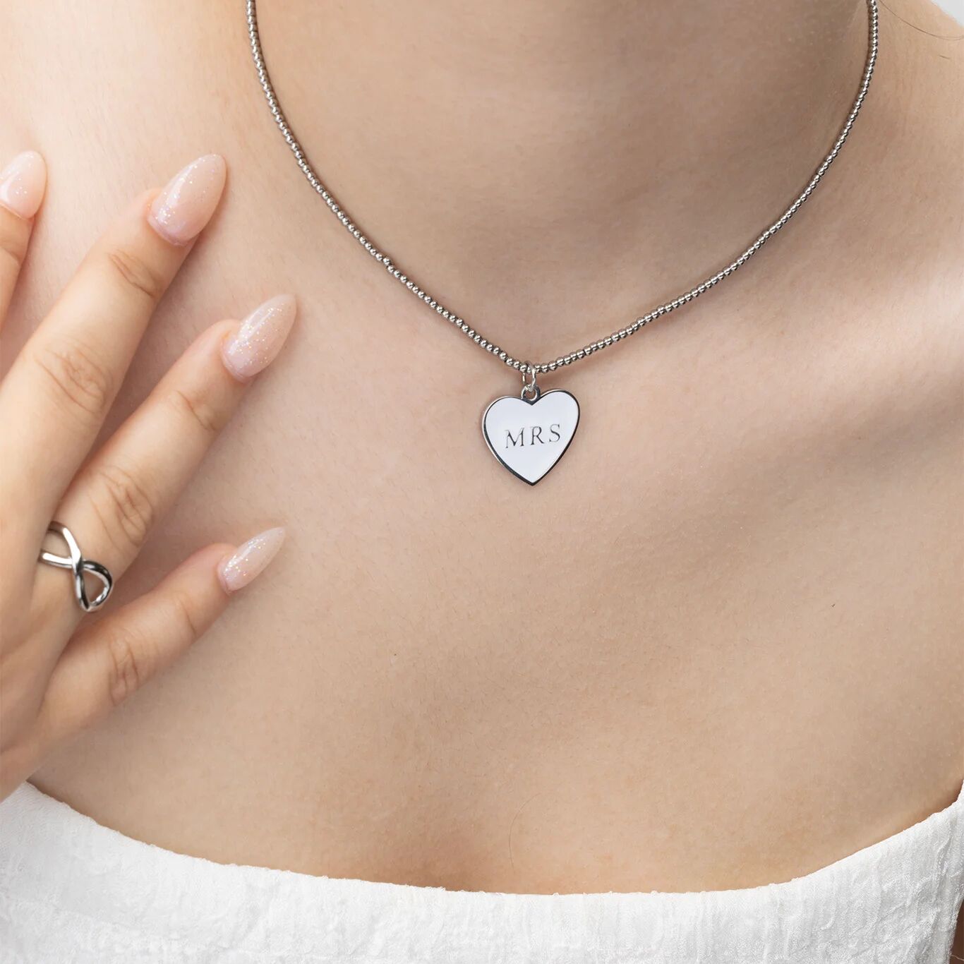 Necklace with a heart-shaped pendant labeled 'MRS' on a person's neck.