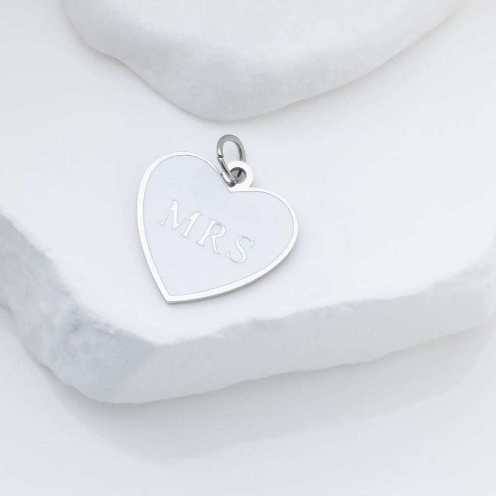 Silver heart-shaped pendant with 'MRS' engraving on a marble surface