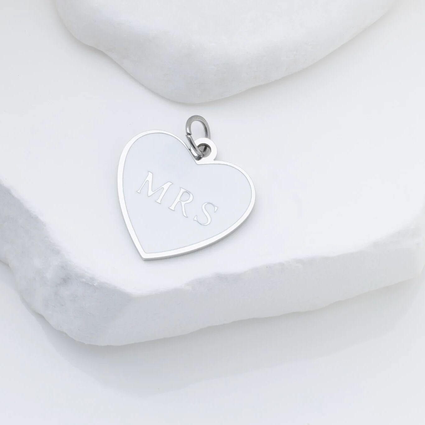 Silver heart-shaped pendant with 'MRS' engraving on a marble surface
