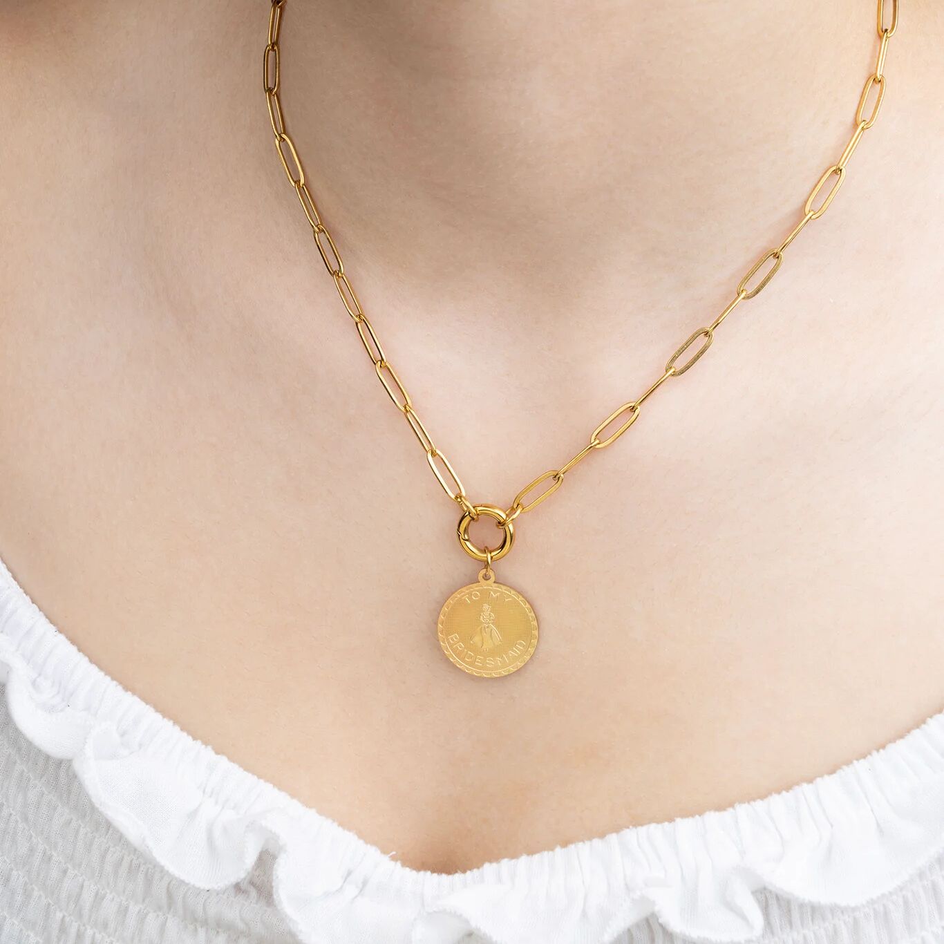 Gold chain necklace with a round pendant on a person wearing a white top.