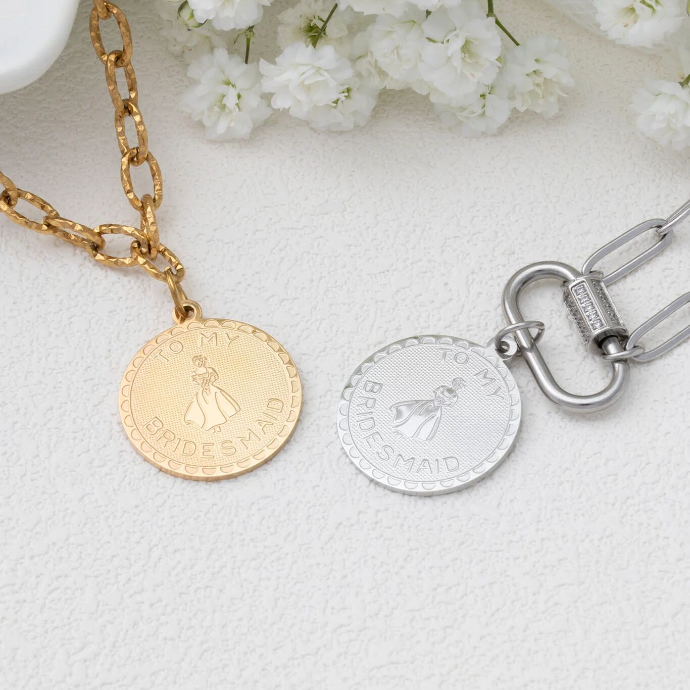Gold and silver necklaces with engraved designs on a light background with white flowers.