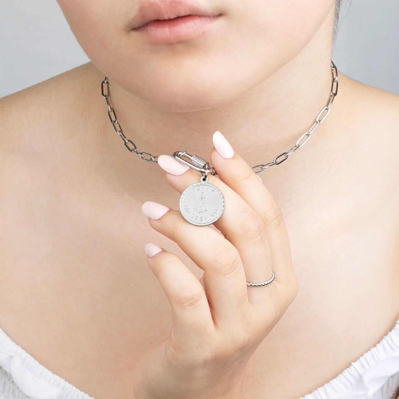 Close-up of a person wearing a silver necklace with a round pendant on a plain background