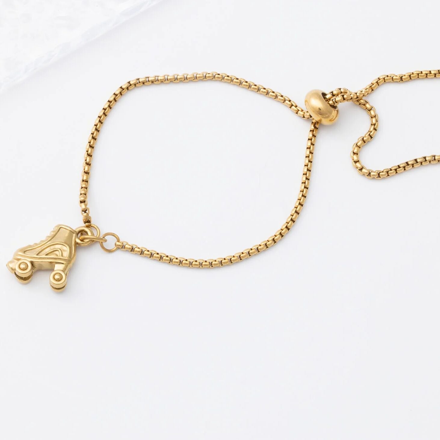 Gold bracelet with a roller skate charm on a white background