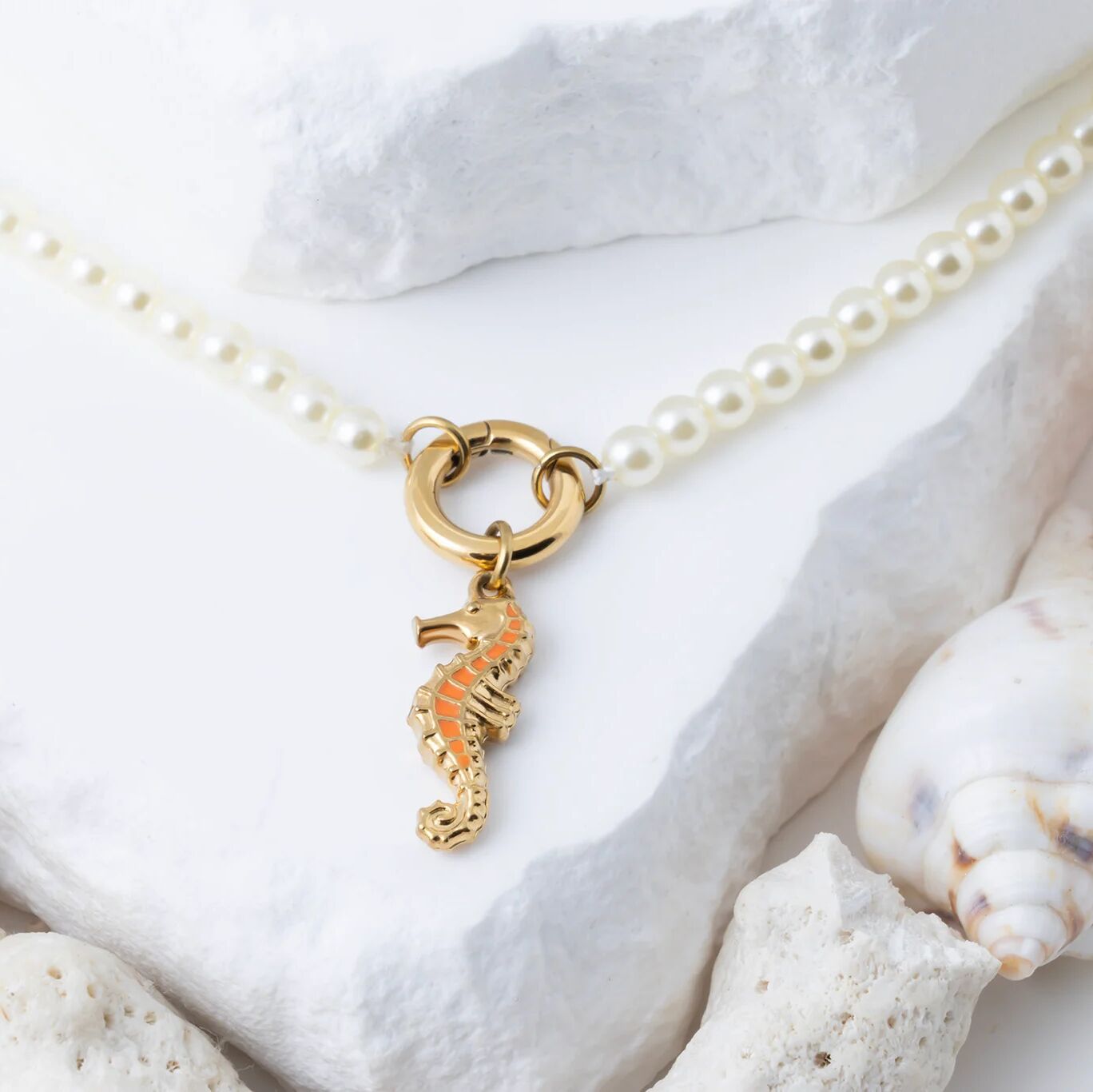 Pearl necklace with a gold seahorse charm on a white surface with shells.