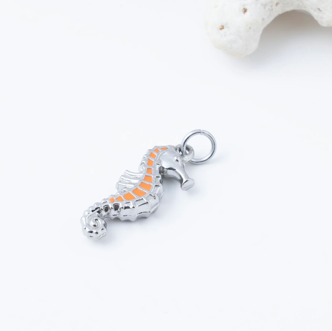 Silver seahorse pendant with orange center on a white background