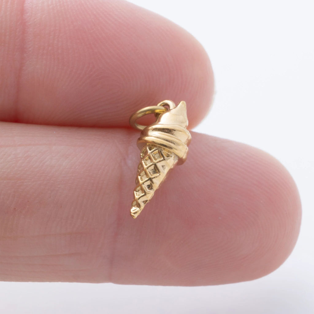 Gold ice cream cone pendant held between fingers on a white background