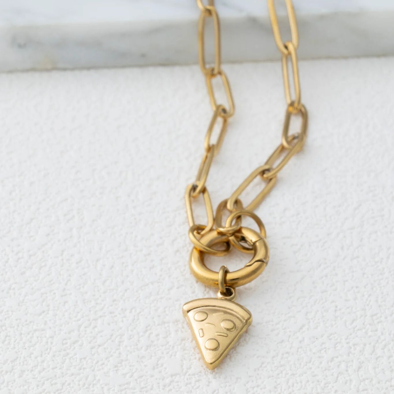 Gold chain necklace with a pizza slice charm on a white marble surface