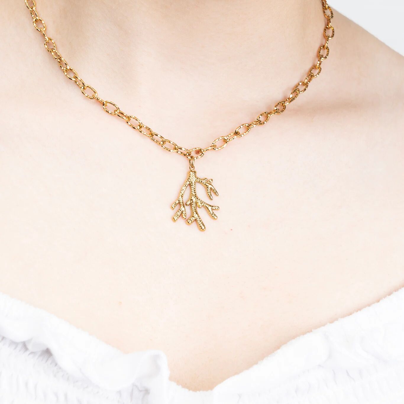Gold necklace with a coral-shaped pendant on a person wearing a white top.