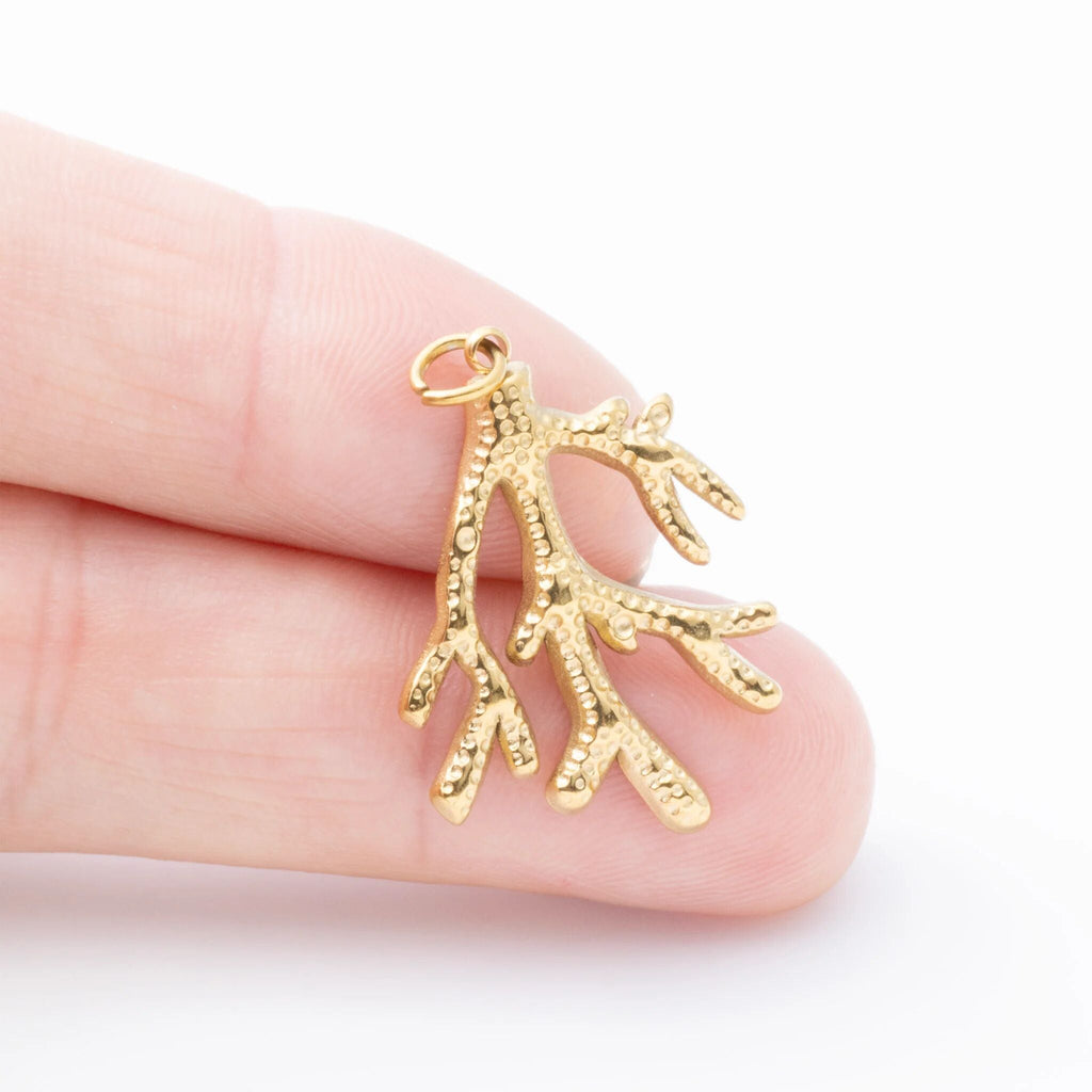 Gold coral-shaped pendant held between fingers on a white background