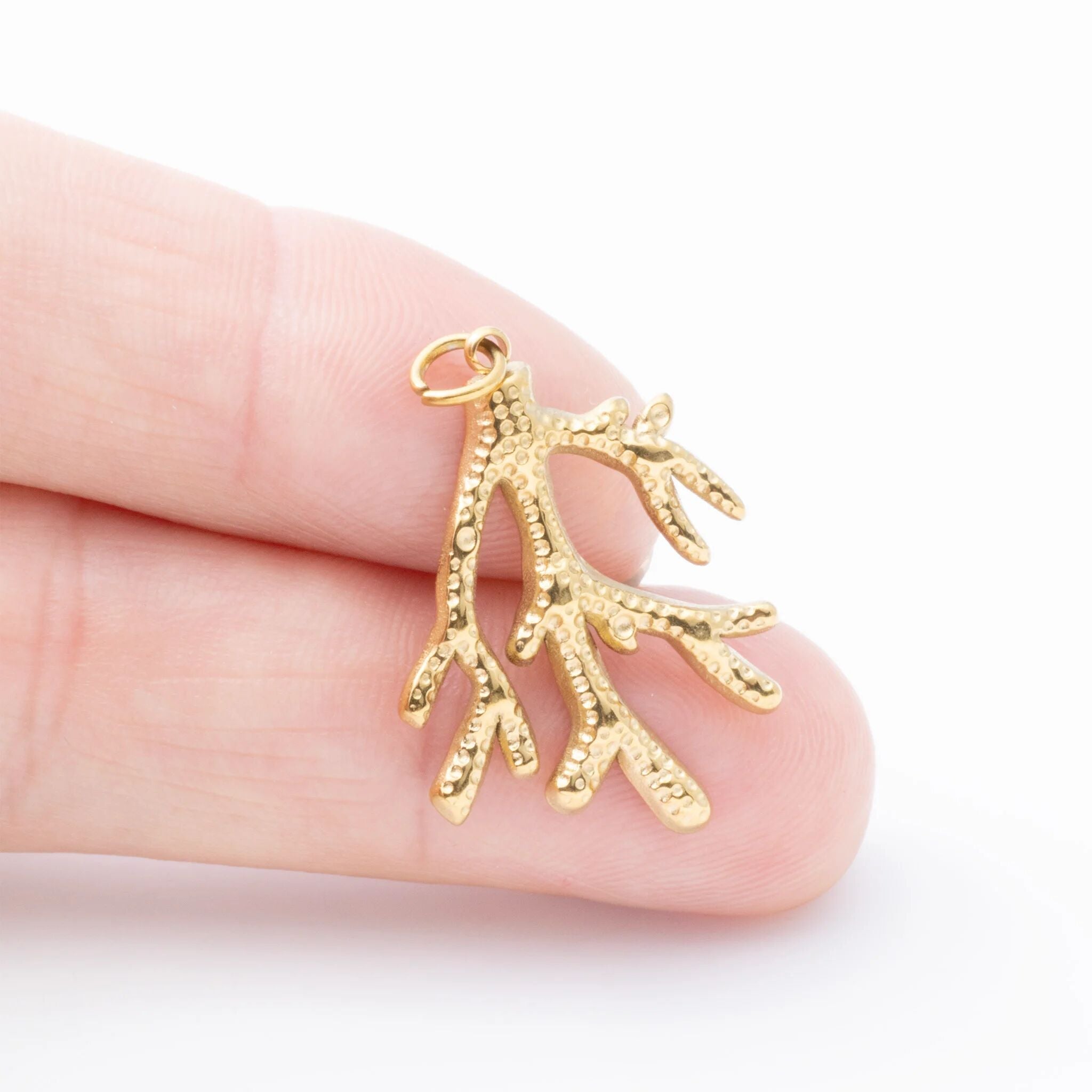 Gold coral-shaped pendant held between fingers on a white background