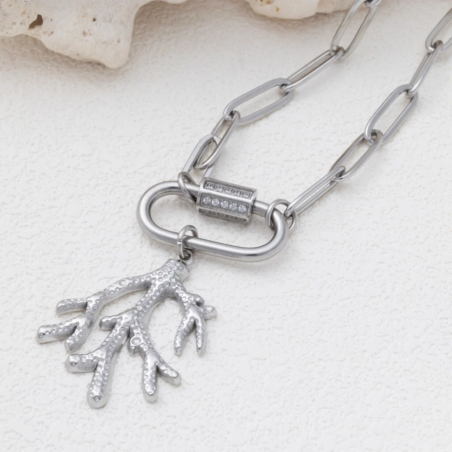 Silver chain necklace with a coral pendant on a light background