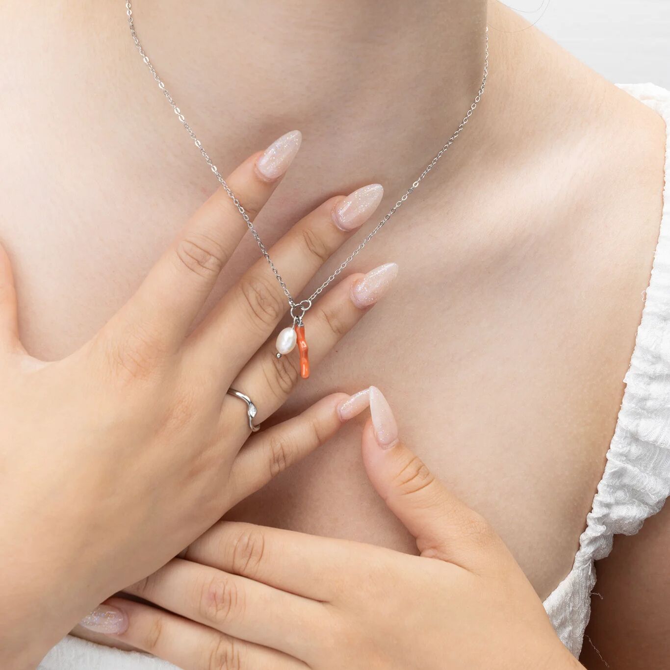 Close-up of a person wearing a silver necklace with a heart pendant and a ring on a plain background