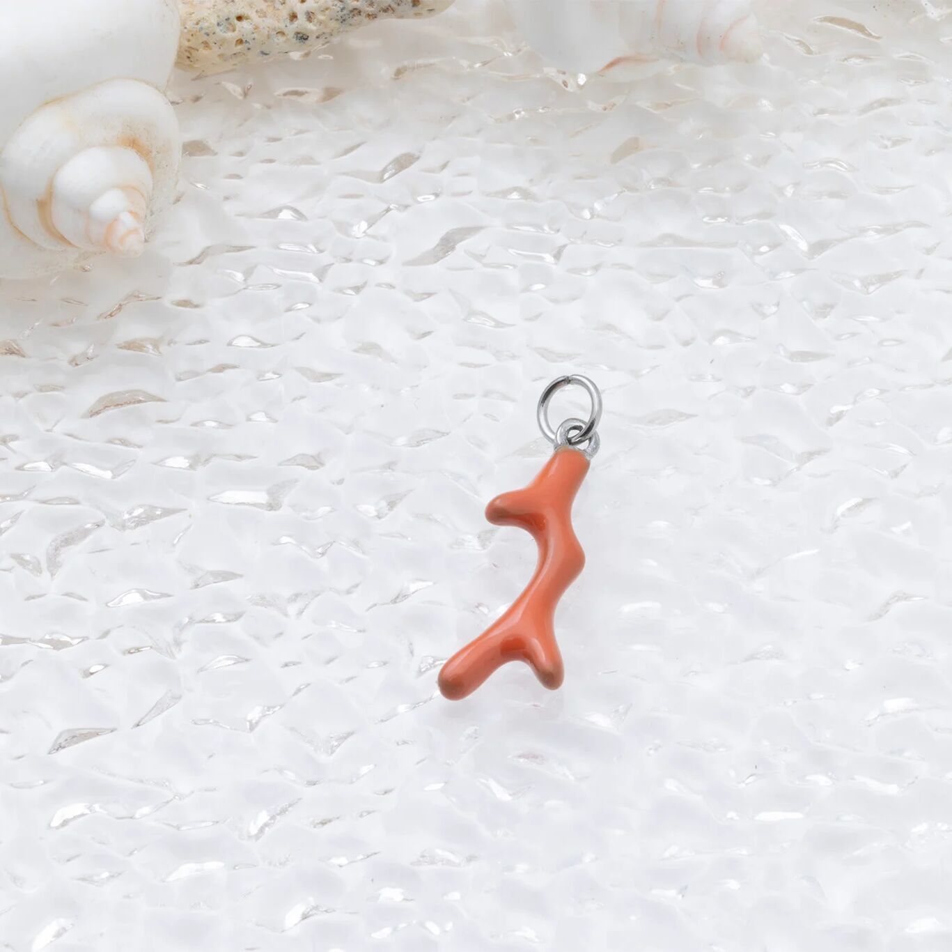 Coral branch charm on a textured white surface with shells in the background
