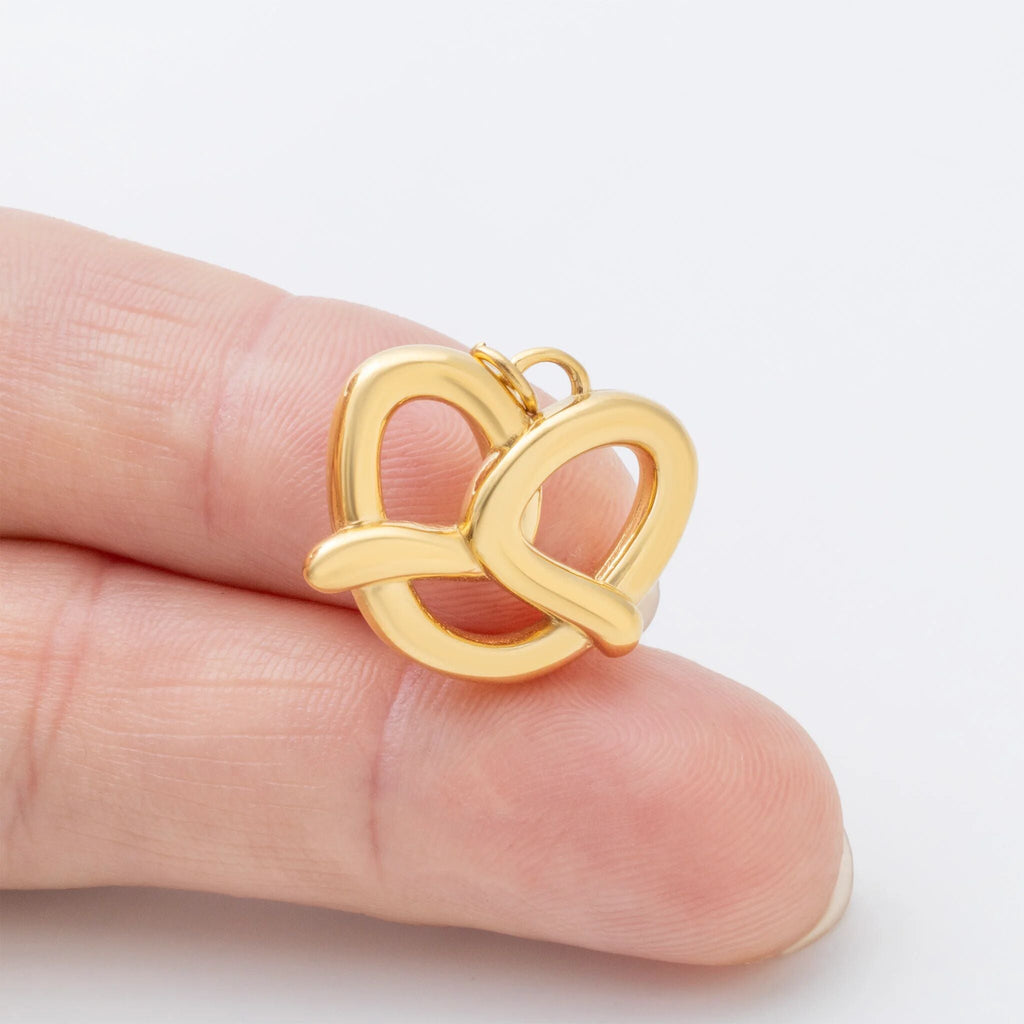 Gold pretzel pendant held between fingers on a white background