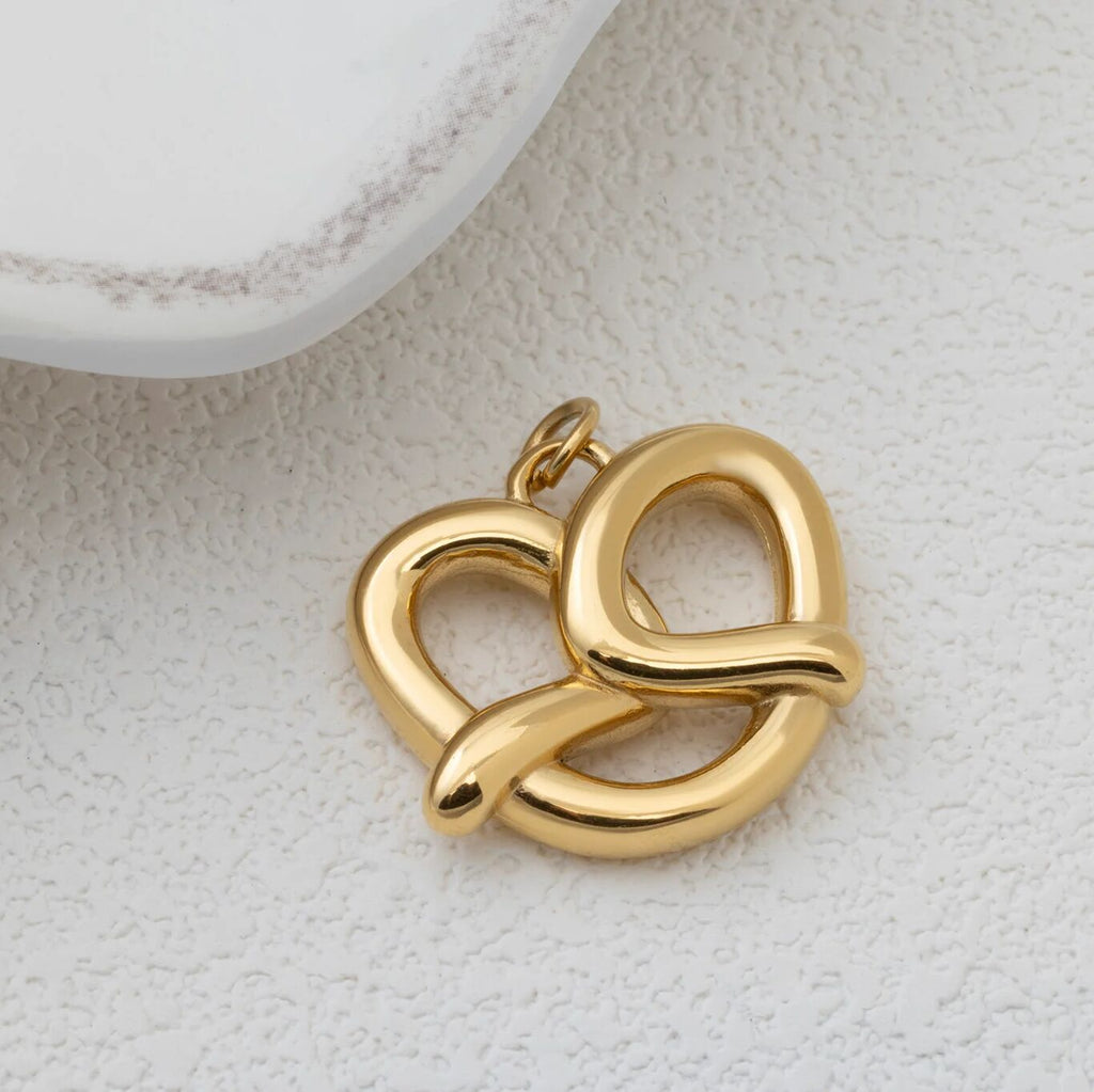 Gold pretzel pendant on a textured beige surface