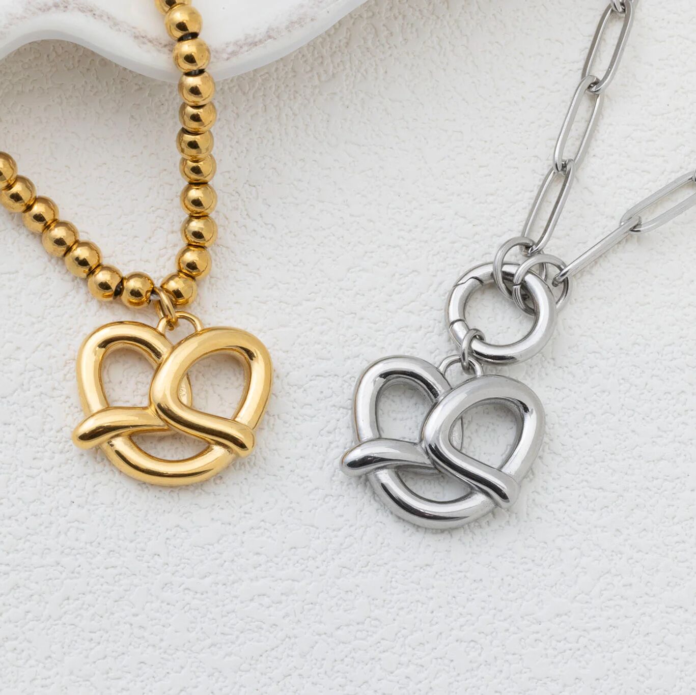 Gold and silver pretzel pendants on chains against a white background