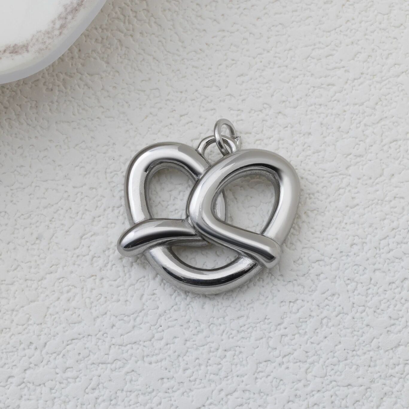 Silver pretzel pendant on a textured white surface