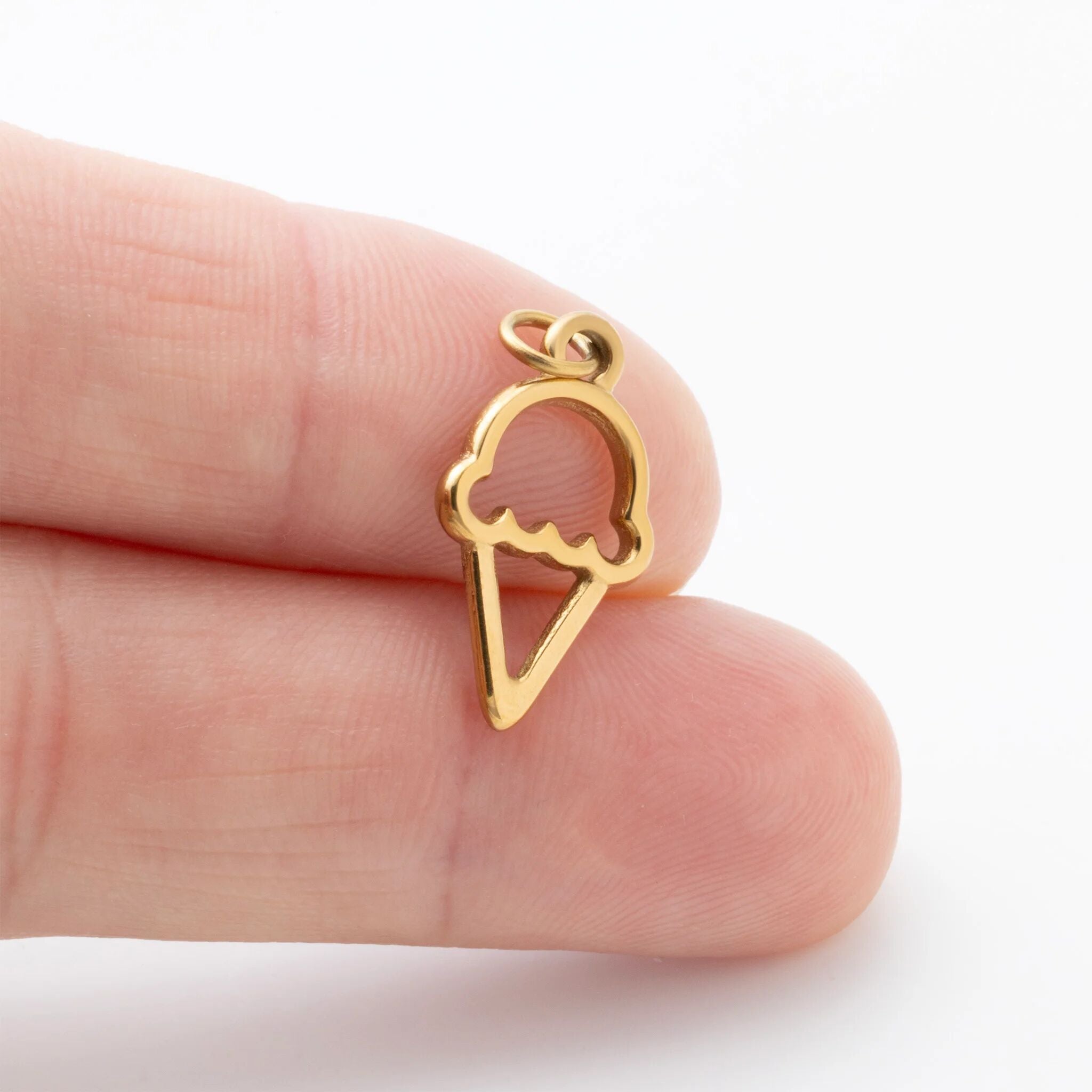 Gold ice cream cone-shaped pendant held between fingers on a white background