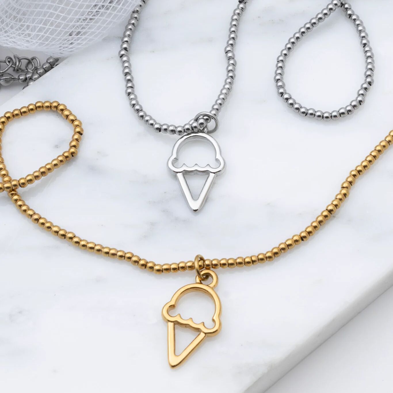Two necklaces with ice cream cone pendants on a marble surface