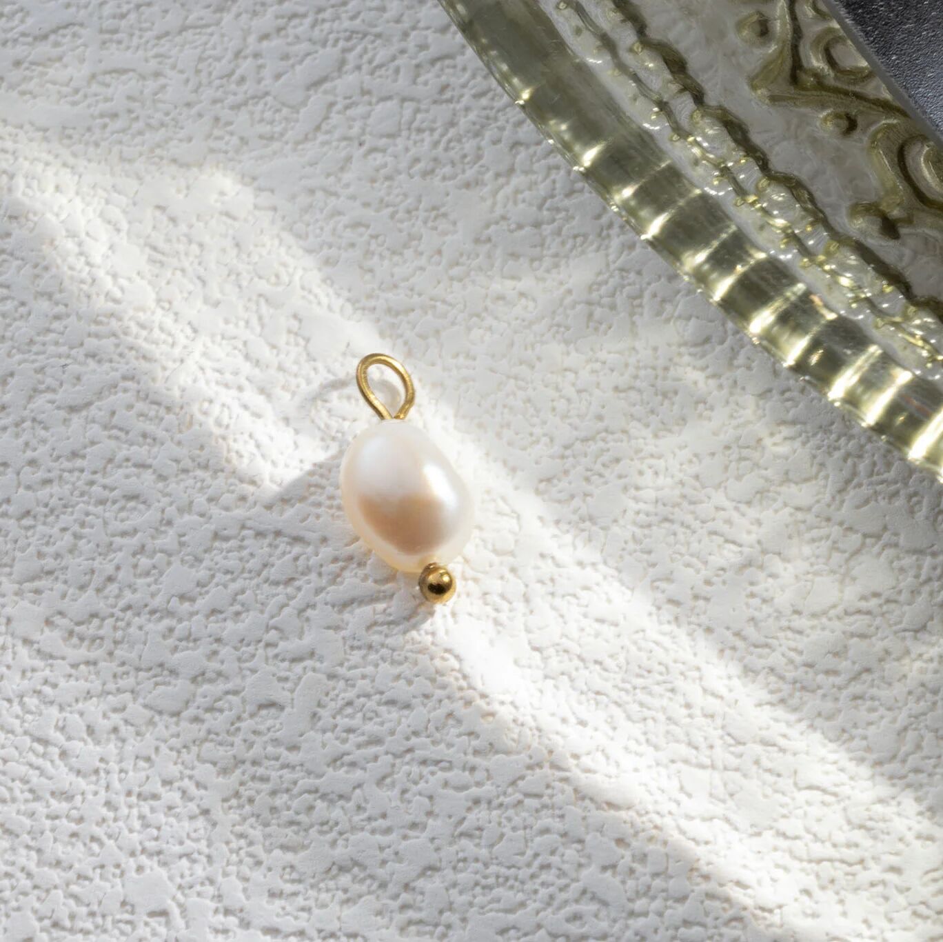 Pearl charm with gold loop on a textured white surface