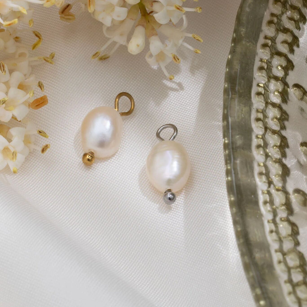 Two pearl charms on a white fabric background with flowers and a decorative object.