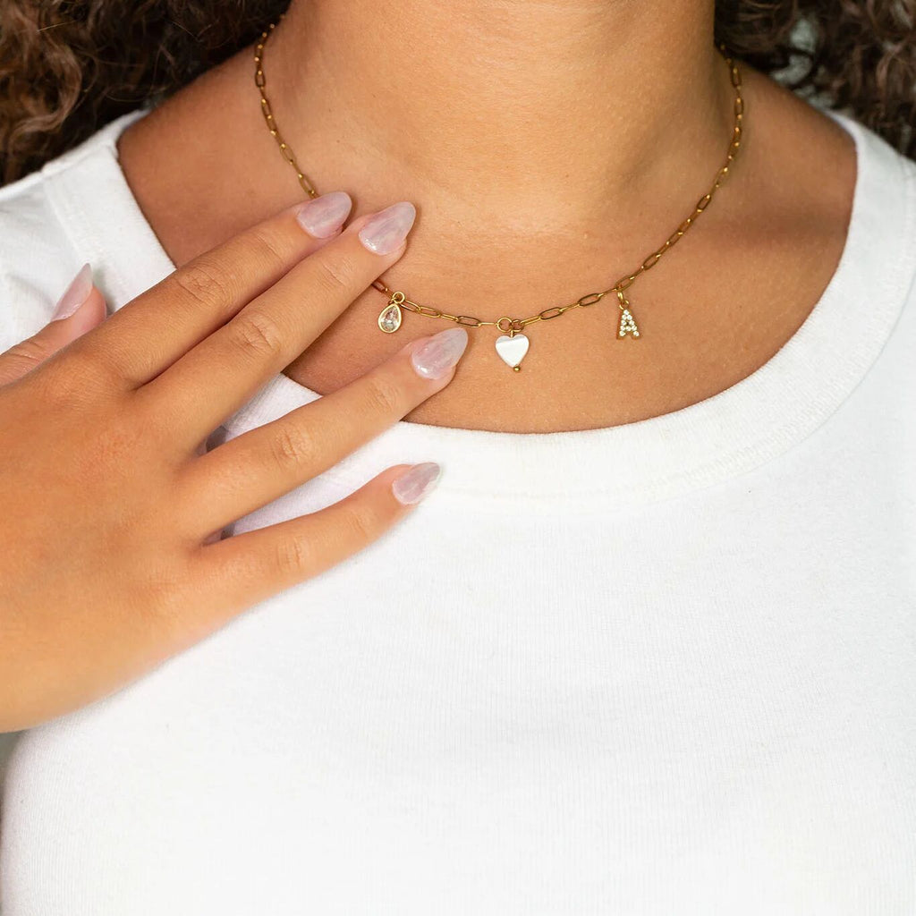Gold necklace with heart and letter 'A' charms worn by a person with a white shirt.
