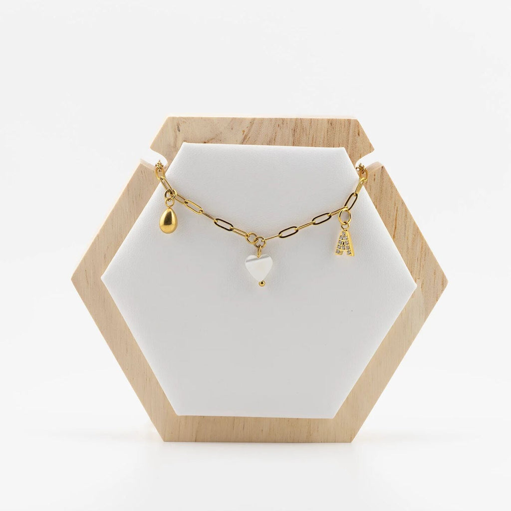 Gold necklace with charms on a white stand with a wooden hexagonal base