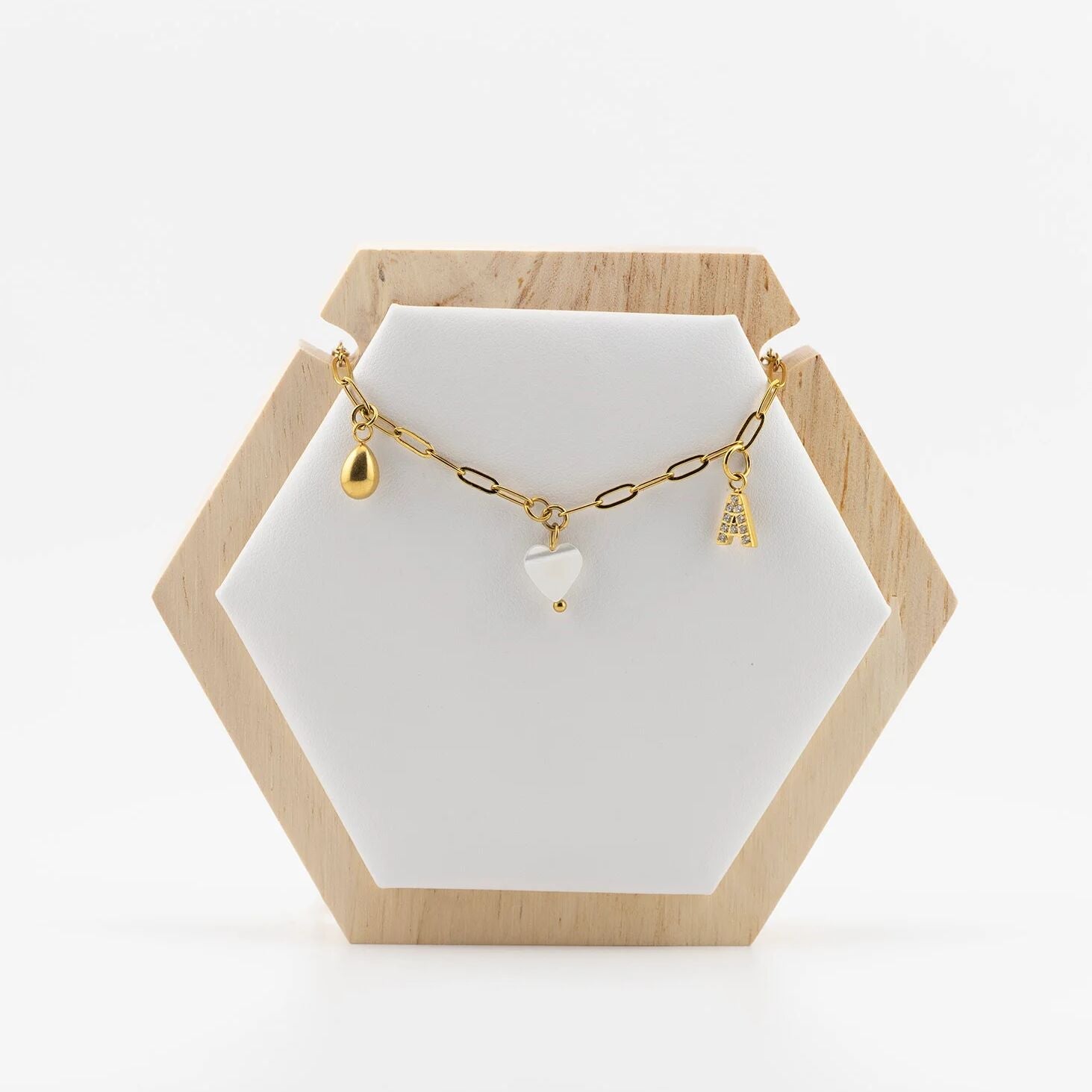 Gold necklace with charms on a white stand with a wooden hexagonal base