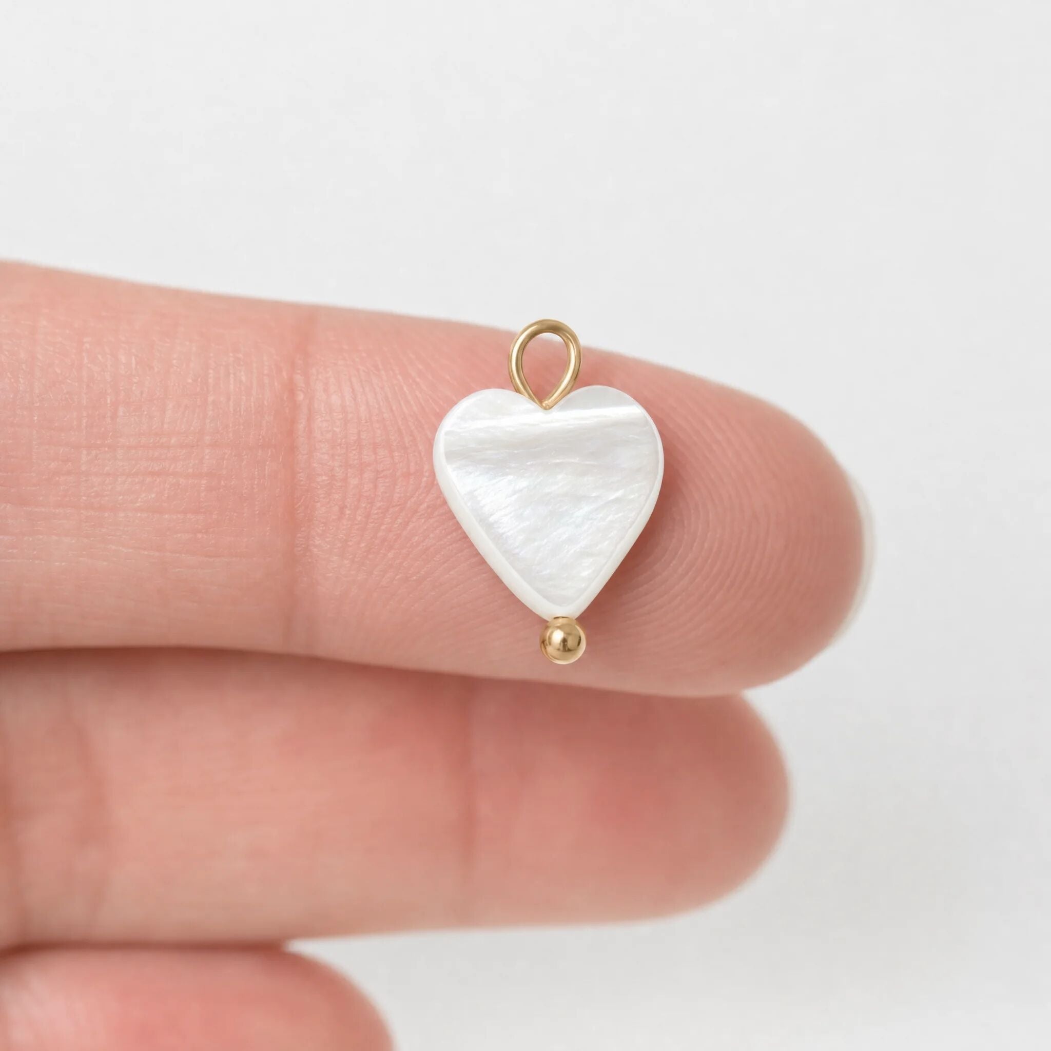 White heart shell pendant with gold accents held between fingers on a light background