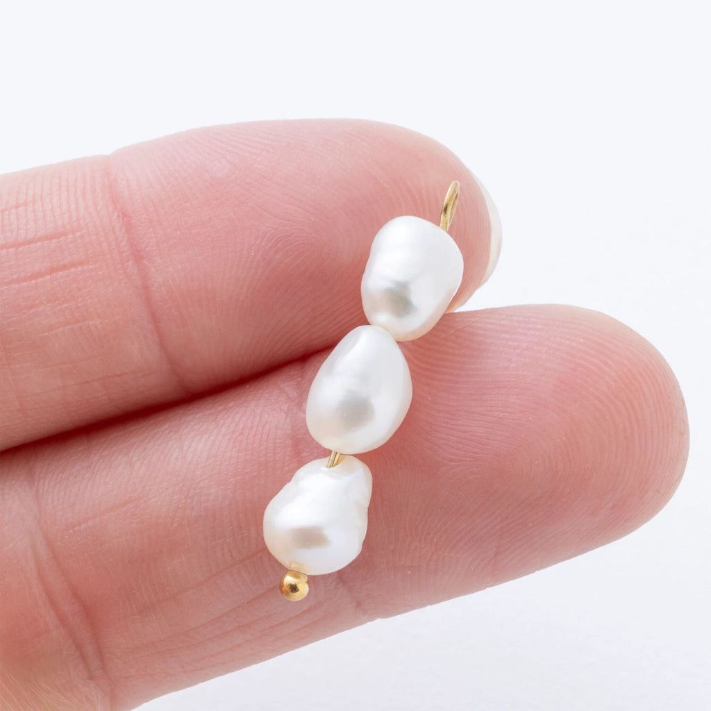 Pearl charm held between fingers on a white background