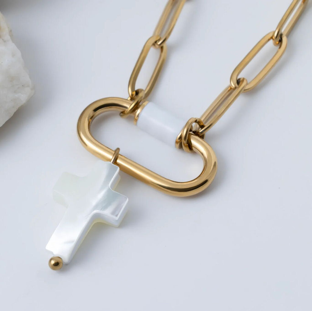 Gold chain necklace with a cross-shaped clasp and white pendant on a light background