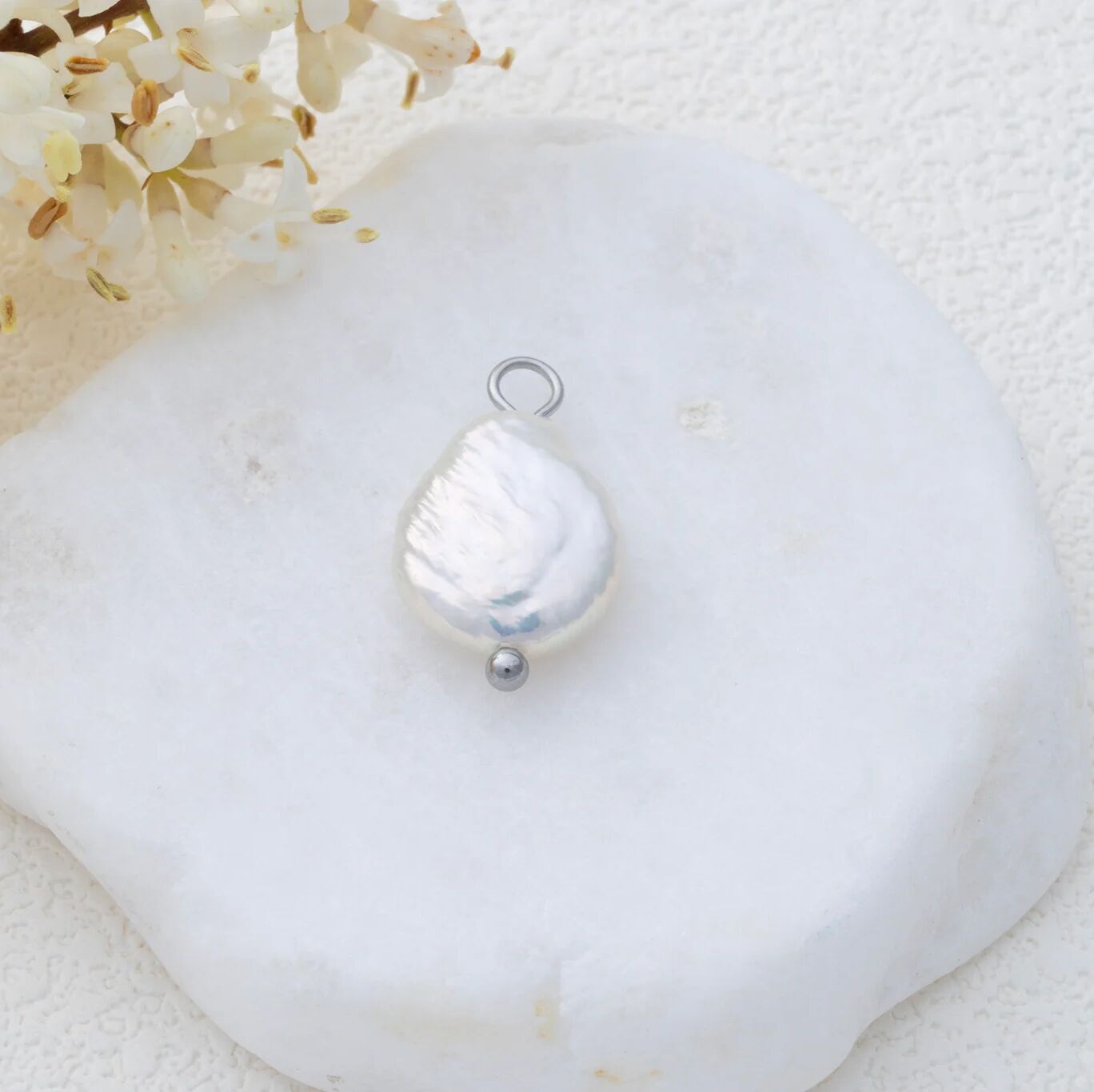 Silver baroque-shaped pendant on a white shell with flowers in the background