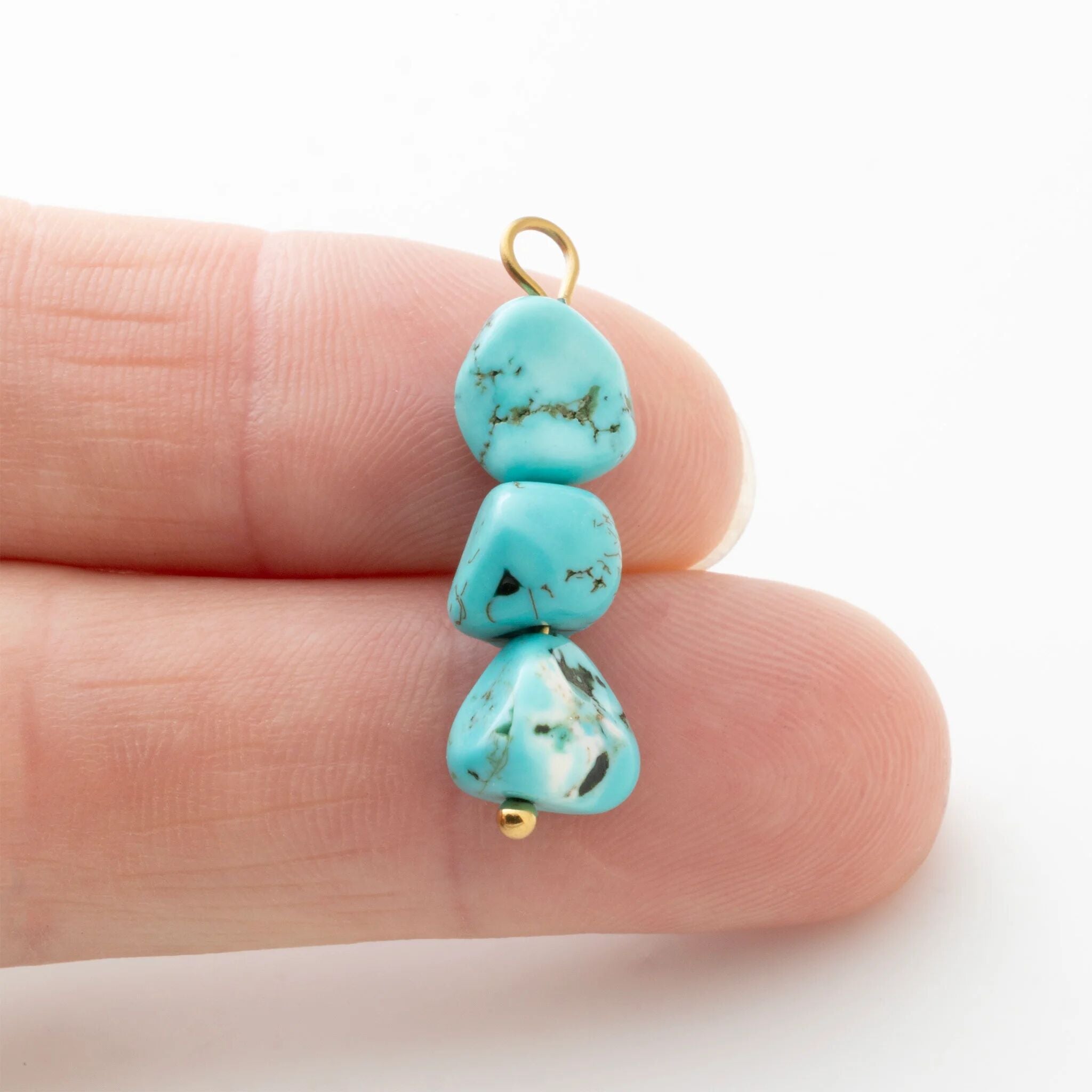 Turquoise stone pendant on a gold chain held between fingers against a white background