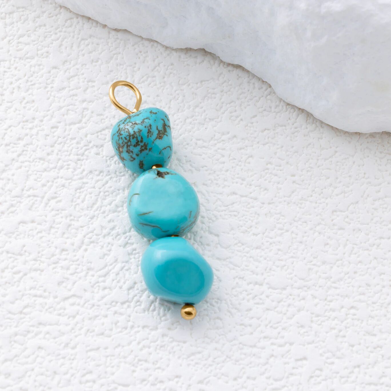 Turquoise bead pendant with gold accents on a textured white surface