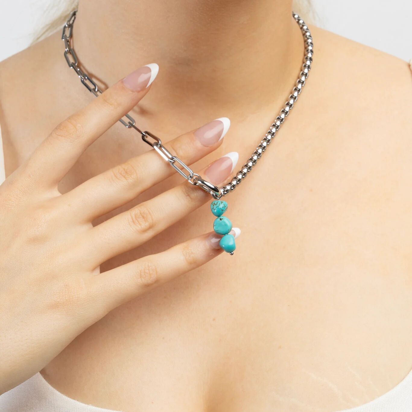 Necklace with turquoise beads being held by a hand against a neutral background