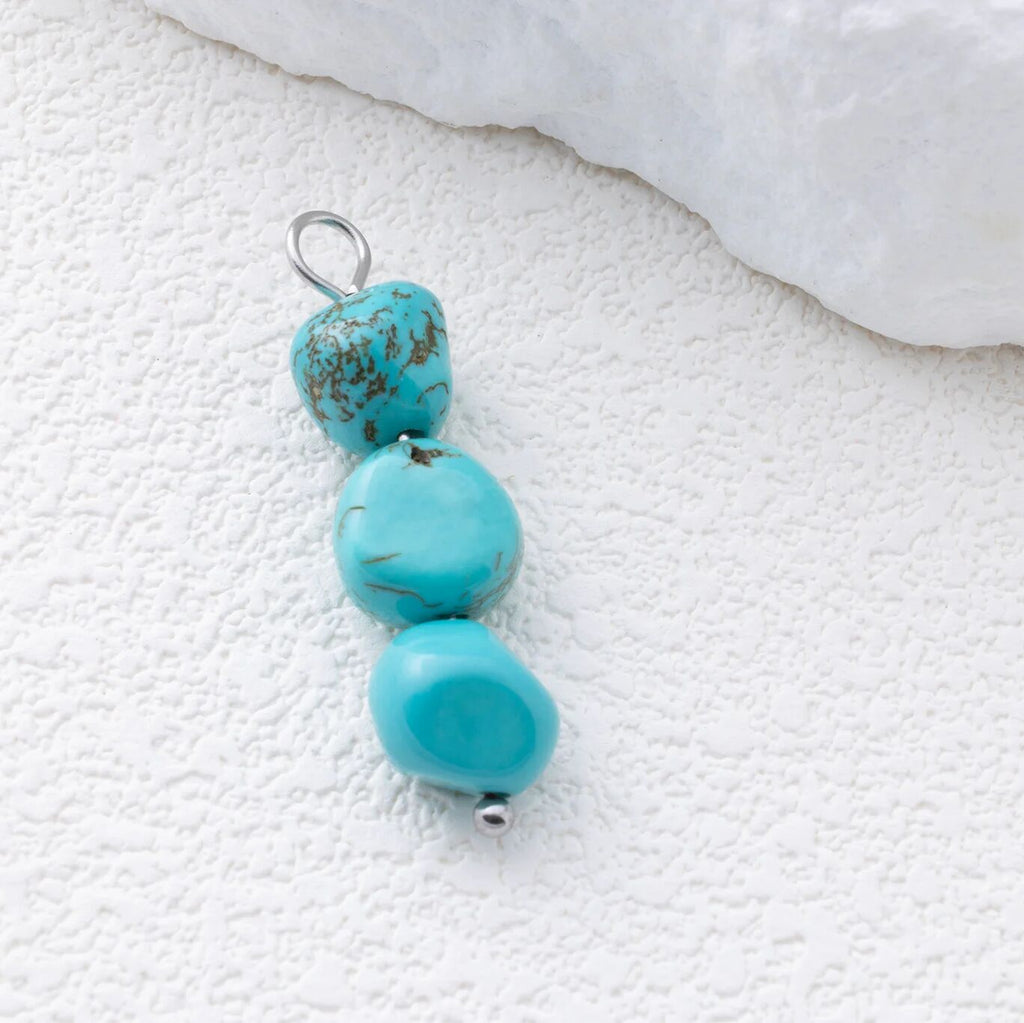 Turquoise bead pendant with gold accents on a textured white surface