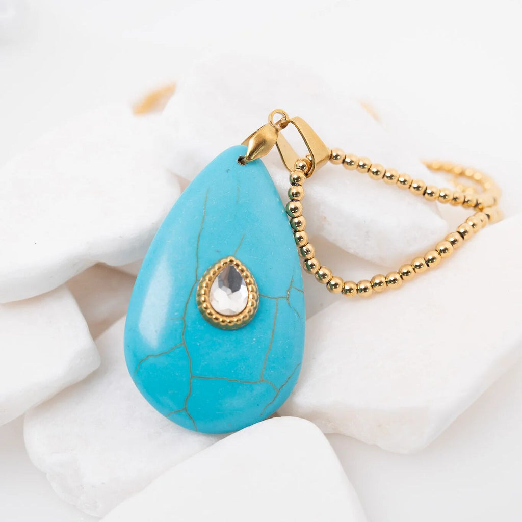 Turquoise teardrop pendant with gold chain on a white background