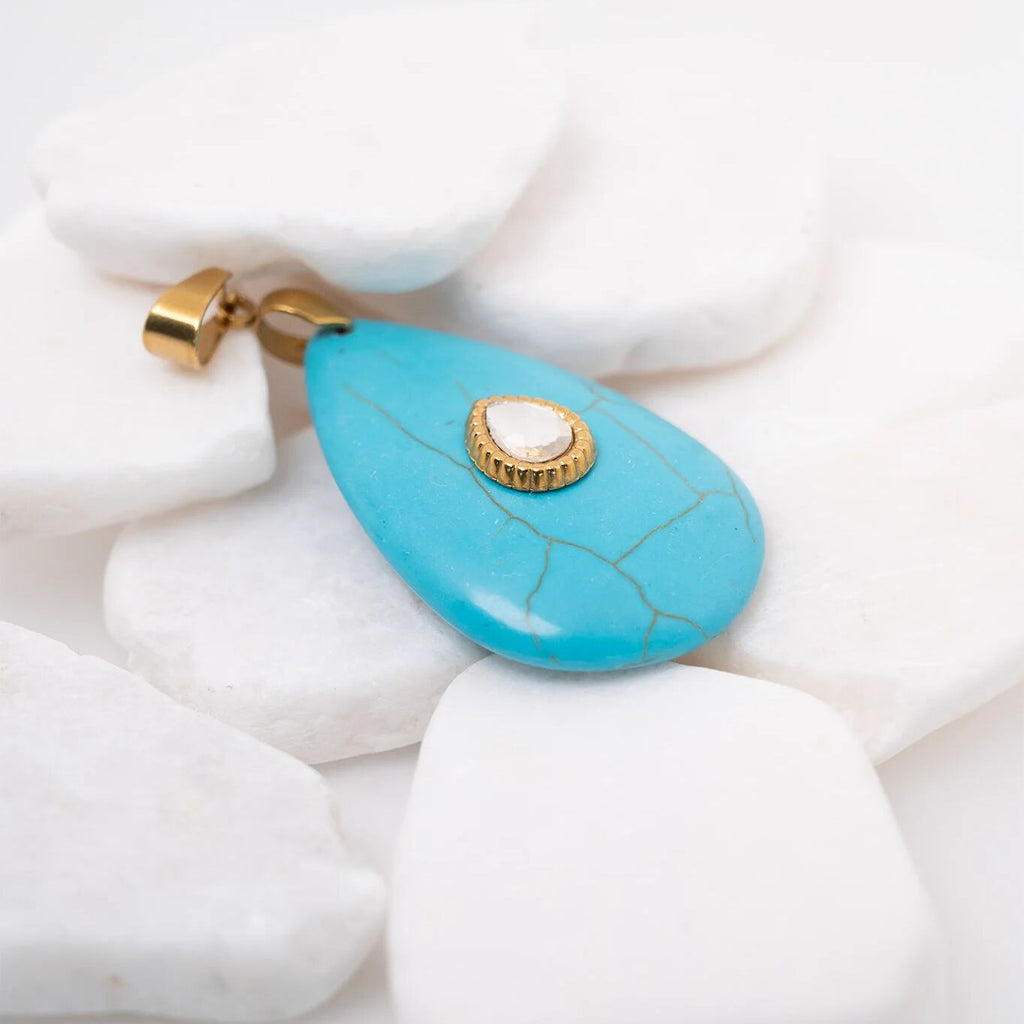 Turquoise teardrop pendant with gold accents on a white stone background