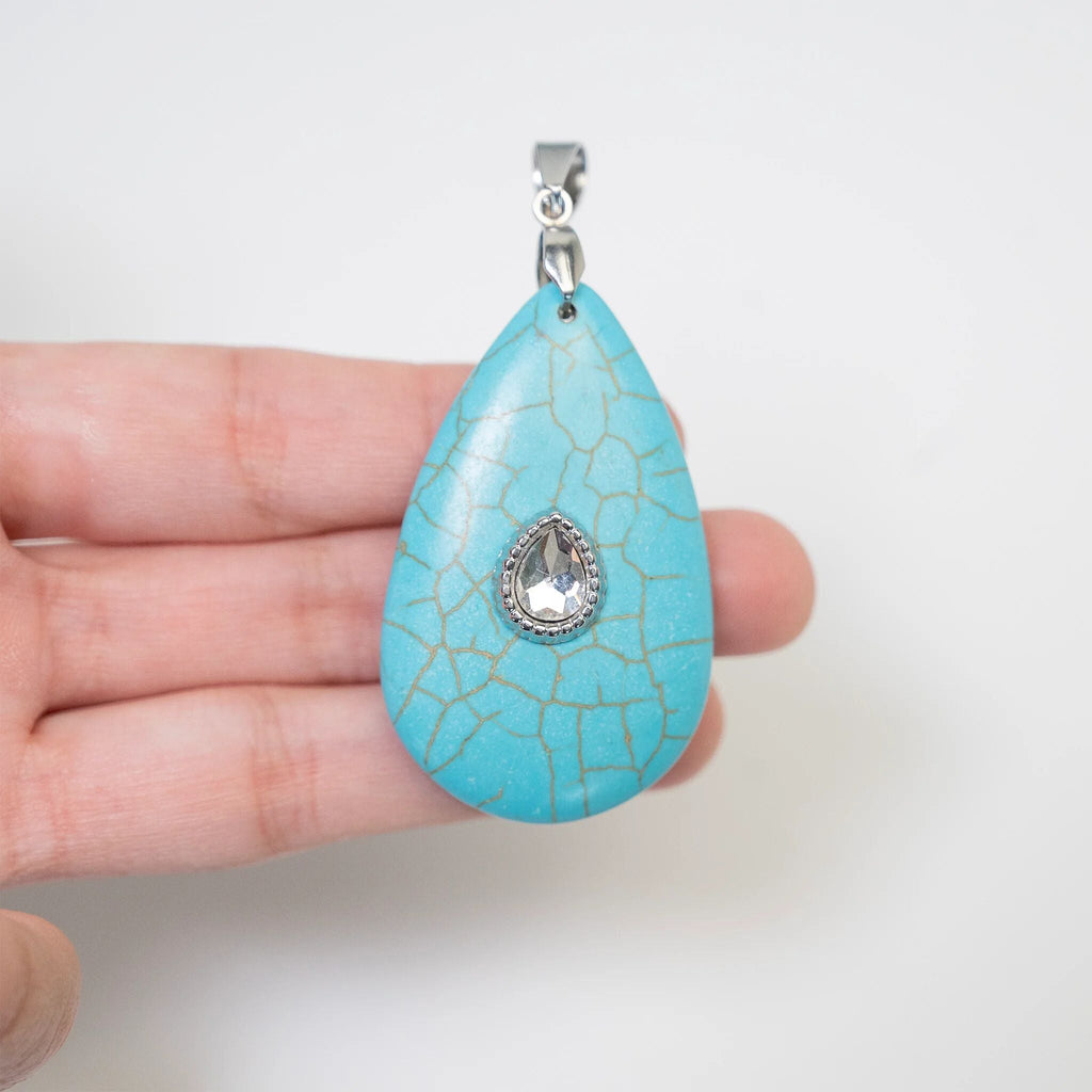 Turquoise teardrop pendant with a silver chain held in a hand against a white background