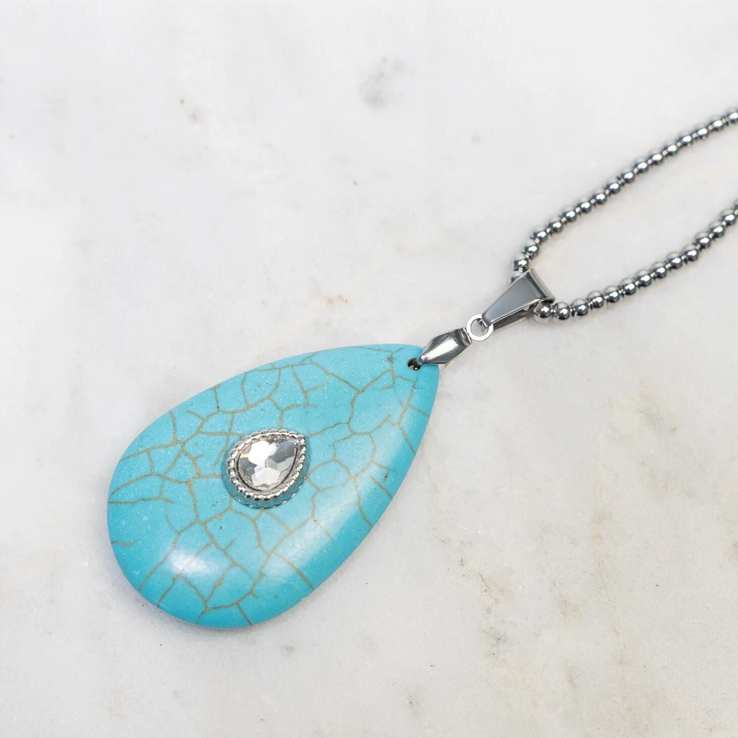 Turquoise teardrop pendant with a silver chain on a marble background