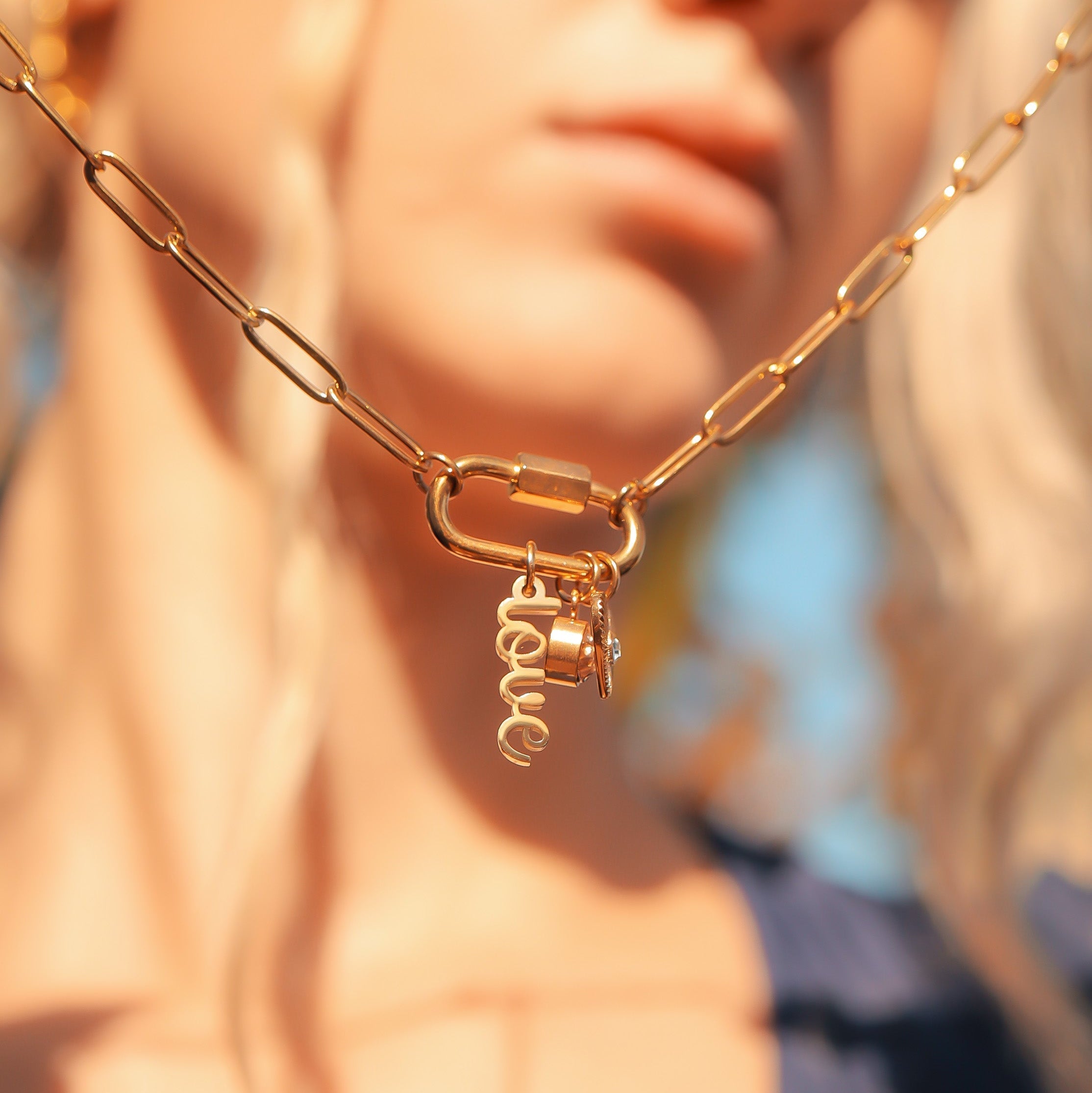 Gold chain necklace with 'love' charm worn by a person outdoors