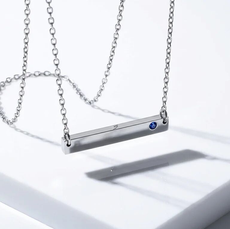 Silver necklace with a bar pendant featuring a blue gemstone on a white surface.