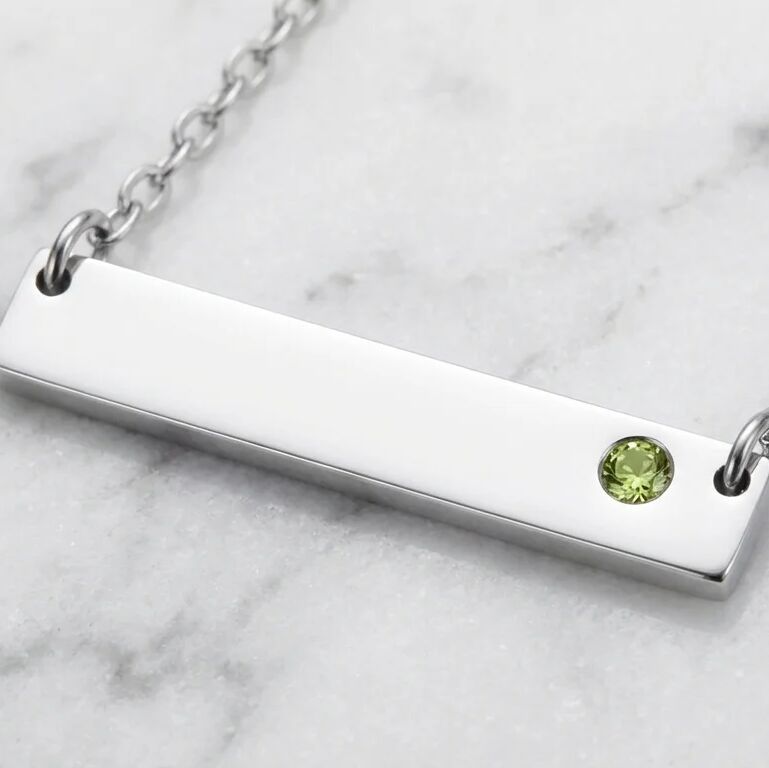 Silver bar necklace with a green gemstone on a marble surface